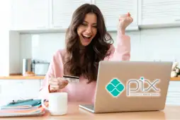 Mulher sorrindo em frente a um computador realizando um Pix com cartão de crédito