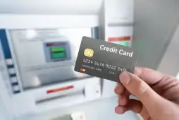 uma mão segurando um cartão em frente a um caixa eletrônico - Como resgatar dinheiro do cartão de crédito