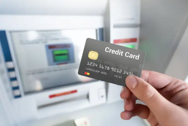 uma mão segurando um cartão em frente a um caixa eletrônico - Como resgatar dinheiro do cartão de crédito